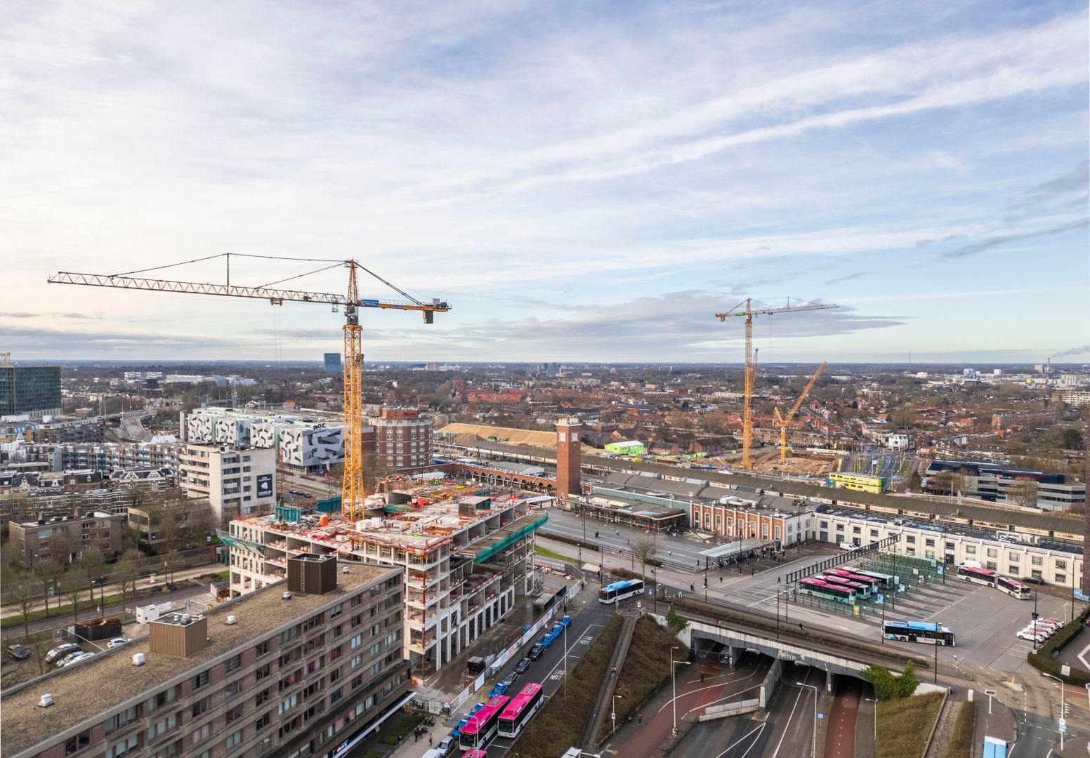 een bouwplaats met daarboven een rode hijskraan